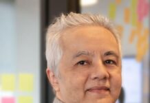 SUTHUB apresenta Conciliahub.ai para ampliar o controle de comissões e repasses em seguros Homem de cabelos grisalhos e camisa cinza sorri em escritório com post-its coloridos ao fundo, em divulgação da SUTHUB